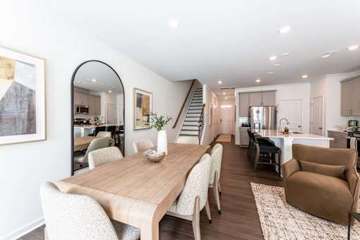Open-concept townhome living, dining, and kitchen area with modern finishes, wood-style flooring, kitchen island, and staircase at Townes at Olde Birch in Raleigh, NC.