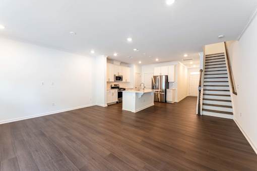 Spacious open-concept townhome living area with wood-style flooring, modern kitchen, stainless-steel appliances, and staircase at Townes at Olde Birch in Raleigh, NC.