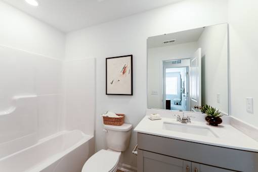 Secondary townhome bathroom with bathtub, vanity, large mirror, and modern neutral finishes at Townes at Olde Birch in Raleigh, NC.