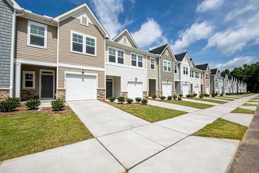 Exterior view of modern townhomes with private garages, driveways, sidewalks, and landscaped lawns at Townes at Olde Birch in Raleigh, NC.
