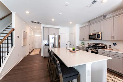 Modern open-concept townhome kitchen with oversized island, stainless-steel appliances, gray cabinetry, and bar seating at Townes at Olde Birch in Raleigh, NC.
