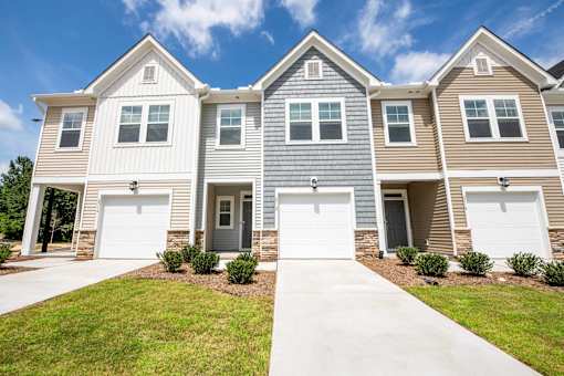 Front exterior of modern two-story townhomes with attached garages, private driveways, stone accents, and landscaped entrances at Townes at Olde Birch in Raleigh, NC.