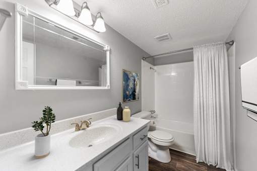 A white bathroom with a sink, mirror, toilet, and shower.