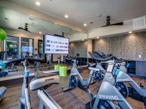 a gym with cardio bikes and a large screen