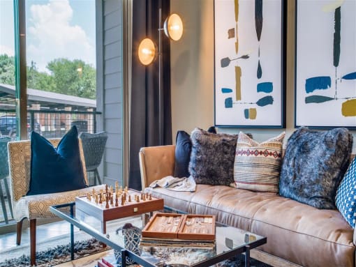 Apartments for Rent Grand Prairie, TX - Waters Edge at Mansfield - Living Room With Floor Lamp, Couch, Chair, Glass Coffee Table, Balcony Doors, and Wall Art.