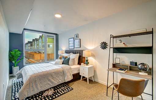 One Bedroom Apartments in West Seattle WA - Upton Flats - Spacious Bedroom wtih Carpetted Floor, Bed, Nightstands with Lamps, Desk, Large Window, and House Plant