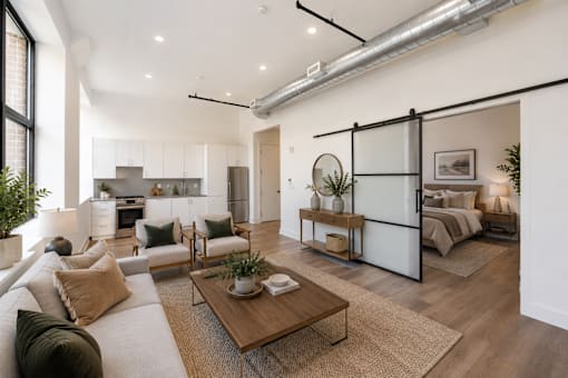 A modern living room with a large sofa, a coffee table, and a bedroom in the background.