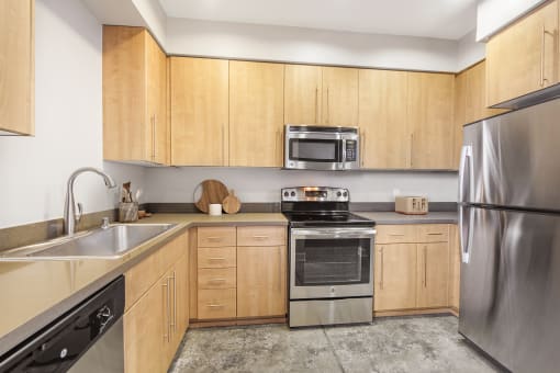 2 Bedroom Modern Apartments in Long Beach, CA - Urban Village - Kitchen with Stained Concrete Flooring, Light Wood Cabinetry, Stainless Steel Appliances, and Quartz Countertops.