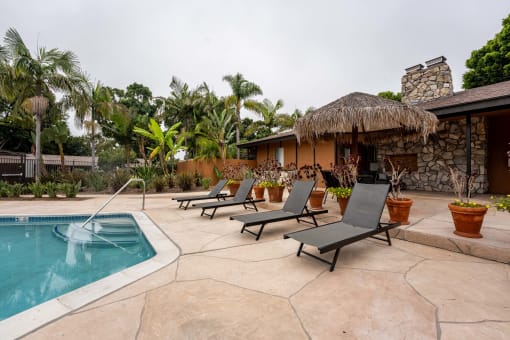 a pool and lounge chairs in front of a house with a thatched roof