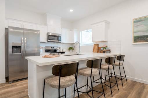 Dog-Friendly Townhomes in Tolleson, AZ - Villas at 91st - Bright White Kitchen With Quartz Island Seating, Shaker Cabinets, and Stainless Steel Refrigerator Appliances.
