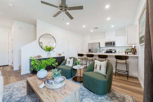 Brand-New Townhomes for Rent in Tolleson, AZ - Villas at 91st - Open-Concept Living Room and Kitchen With Ceiling Fan, Recessed Lighting, Armchairs, Coffee Table, and Breakfast Bar Seating.