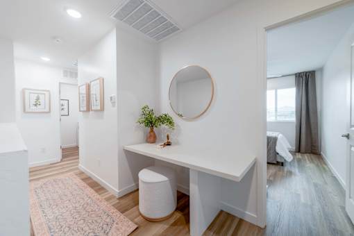 A white room with a round mirror and a desk with a plant on it.