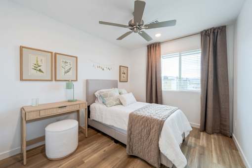 A bedroom with a bed, a desk, and a ceiling fan.