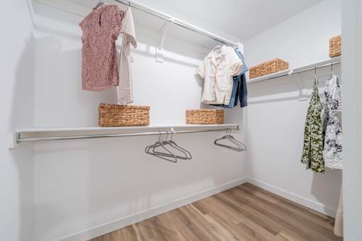 A white closet with clothes hanging and baskets on the shelf.