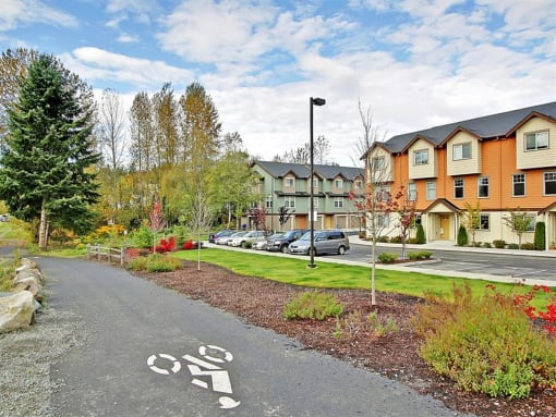 Kenmore, WA, Apartments for Rent - Northshore Townhomes - Bike Path and Building Exterior with View of Parking Lot and Surrounded by Beautiful Landscaping and Trees.