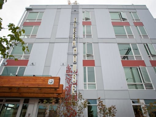 South Seattle, WA, Apartments - Greenhouse - Property Exterior with Grey Walls, Red and Wooden Details, and Trees.