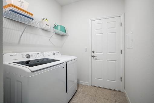 A white Samsung dishwasher and dryer are in a small laundry room with a white door.
