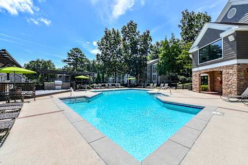 A large swimming pool surrounded by a concrete patio and lounge chairs.