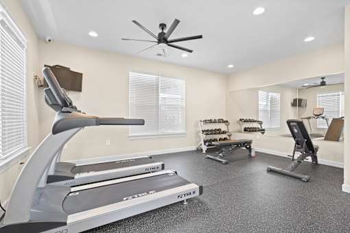 Spacious fitness center at Hawks Landing Apartments in Hickory, NC with treadmills, ellipticals, and ceiling fan