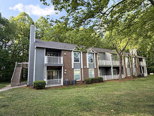 Apartment building with a grey and brown exterior and a tree in front.