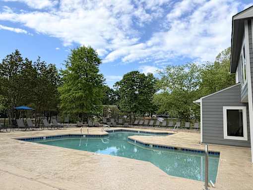 A pool surrounded by trees and chairs.