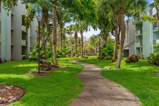 a path through the grass and trees in front of an apartment building