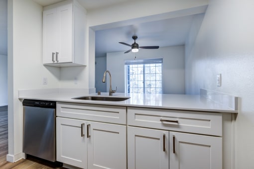 One-Bedroom Apartments in Everett, Washington - Woodbrook - Kitchen with Wood-Style Flooring, Stainless Steel Dishwasher, Sleek White Cabinets, and Breakfast Bar.