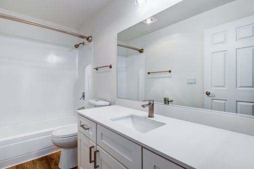 Everett, Washington, Apartments - Woodbrook - Bathroom with Wood-Style Flooring, Shower and Tub Combo, Oversized Mirror, Sink Vanity with Modern Hardware, and White Cabinetry.