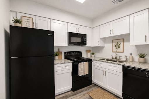 A black refrigerator sits next to a black stove in a kitchen with white cabinets.