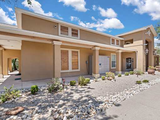 A modern house with a beige exterior and a gravel driveway.