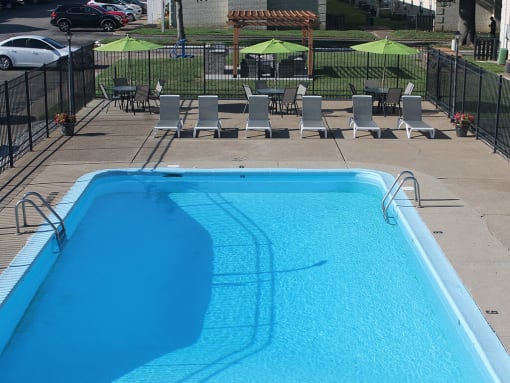 a large pool with chairs and umbrellas with a grilling area in the background