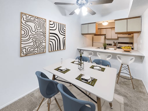 a dining area with a table and chairs and a kitchen in the background