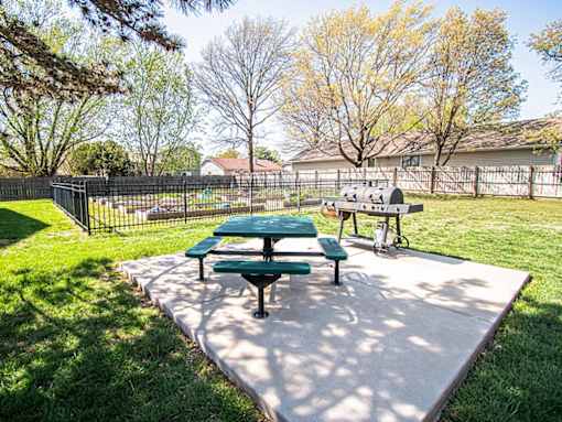 A green picnic table and bench are in a sunny park.