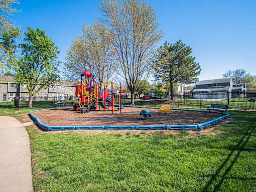 A playground with a blue rubberized surface and a red and yellow slide.