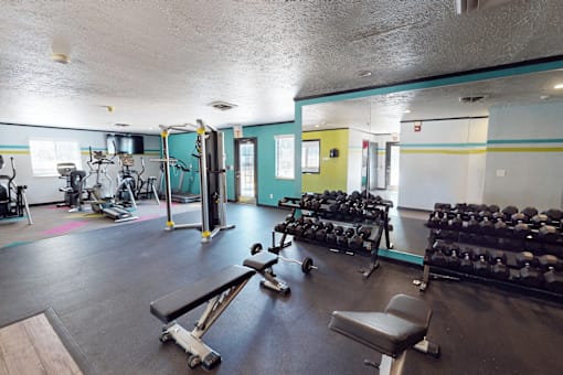 A gym with a variety of equipment including weights and a bench.