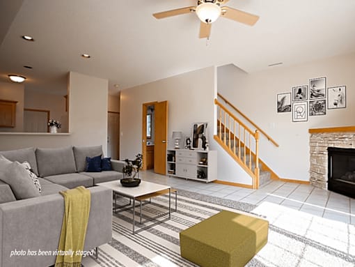 A living room with a grey couch, a yellow ottoman, and a fireplace.