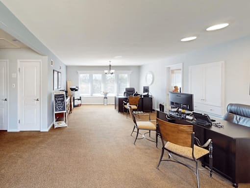 A living room with a brown carpet and a black desk.