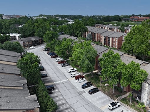 A parking lot with cars and trees in front of apartment buildings.