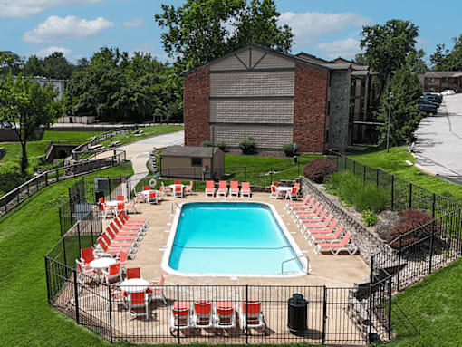 A pool surrounded by red chairs and a black fence.