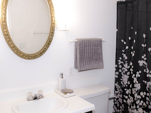 A bathroom with a white toilet, a white sink, a gold framed mirror, and a black and white shower curtain.