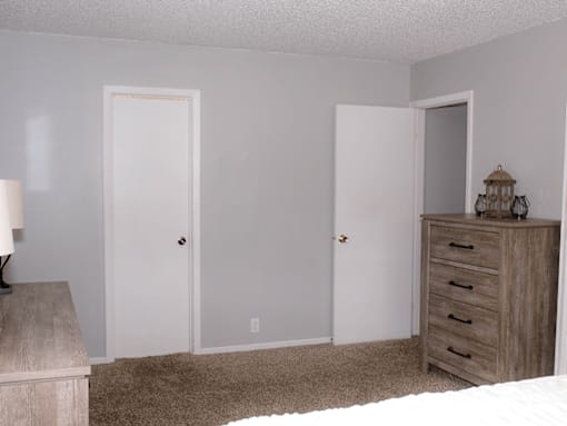 A room with two doors and a dresser with a lamp on top.