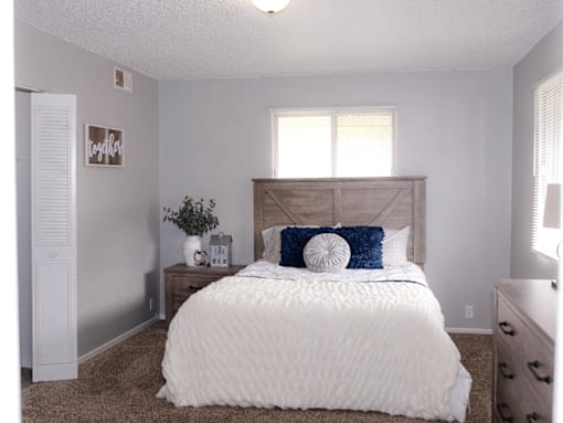A white bed with a blue pillow and a white comforter.