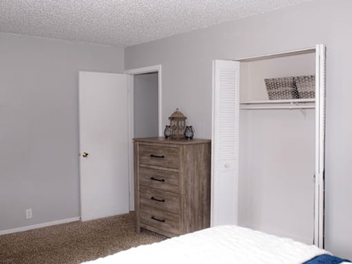 A bedroom with a bed, dresser, and open closet.