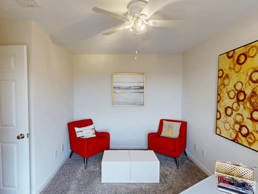 a living room with two red chairs and a ceiling fan