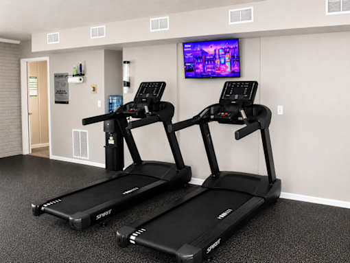 Two treadmills are in a gym with a television mounted on the wall.