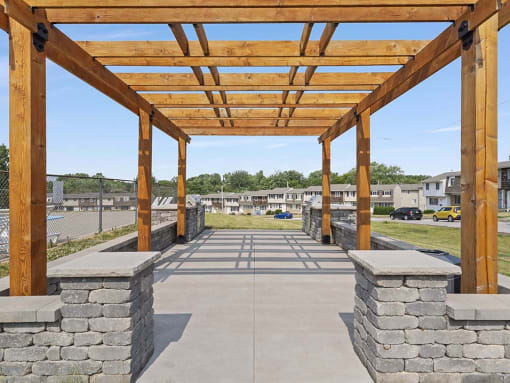 a pergola with stone pillars and a parking lot in the background