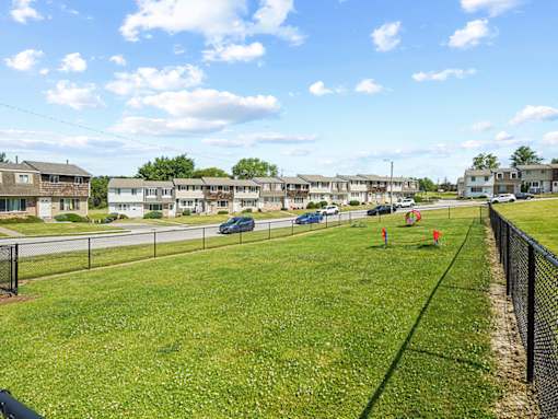 A grassy field with a fence and apartment buildings in the background.