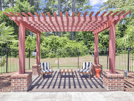 A red pergola with two chairs and a table is in the foreground of a garden.