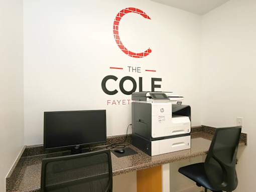 A black monitor and printer on a desk with a black chair.