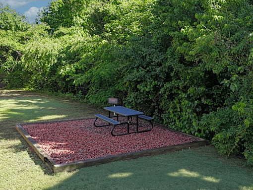 A picnic table is on a red gravel area in a green grassy area.